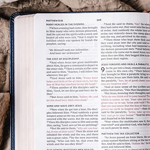 Una Biblia abierta descansa sobre una superficie de tela ligera, en la que se ven pasajes del Evangelio de Mateo, con los títulos visibles, texto resaltado y las palabras de Cristo en rojo.