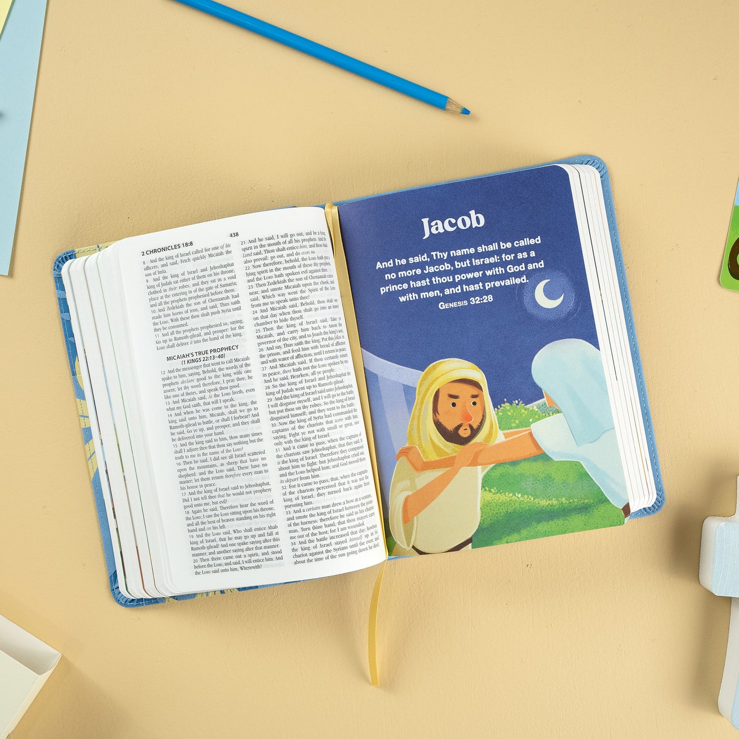 Una Biblia ilustrada abierta muestra una página sobre Jacob, en la que aparece un hombre con un pergamino bajo una luna creciente y, a la derecha, el versículo de Génesis 32:28, ideal para niños de entre 3 y 5 años.