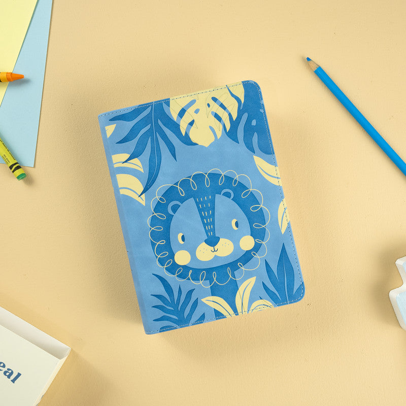 Un cuaderno azul con la cara de un león de dibujos animados y motivos de hojas en la portada descansa sobre una superficie beige, rodeado de lápices de colores y hojas de papel; es perfecto para que los niños de entre 3 y 5 años lo utilicen en actividades como la lectura de una Biblia ilustrada.