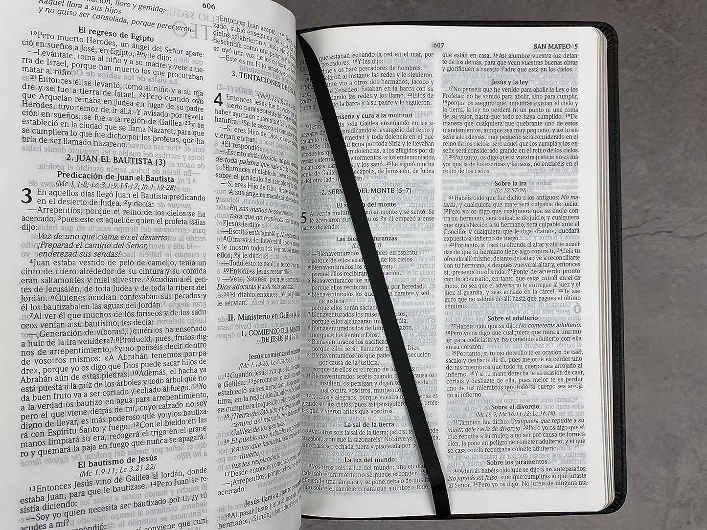 Una Biblia «ultrafina» Reina Valera 2020 en español, abierta, yace sobre una superficie gris, con una cinta negra colocada en diagonal a través de las páginas a modo de marcapáginas.