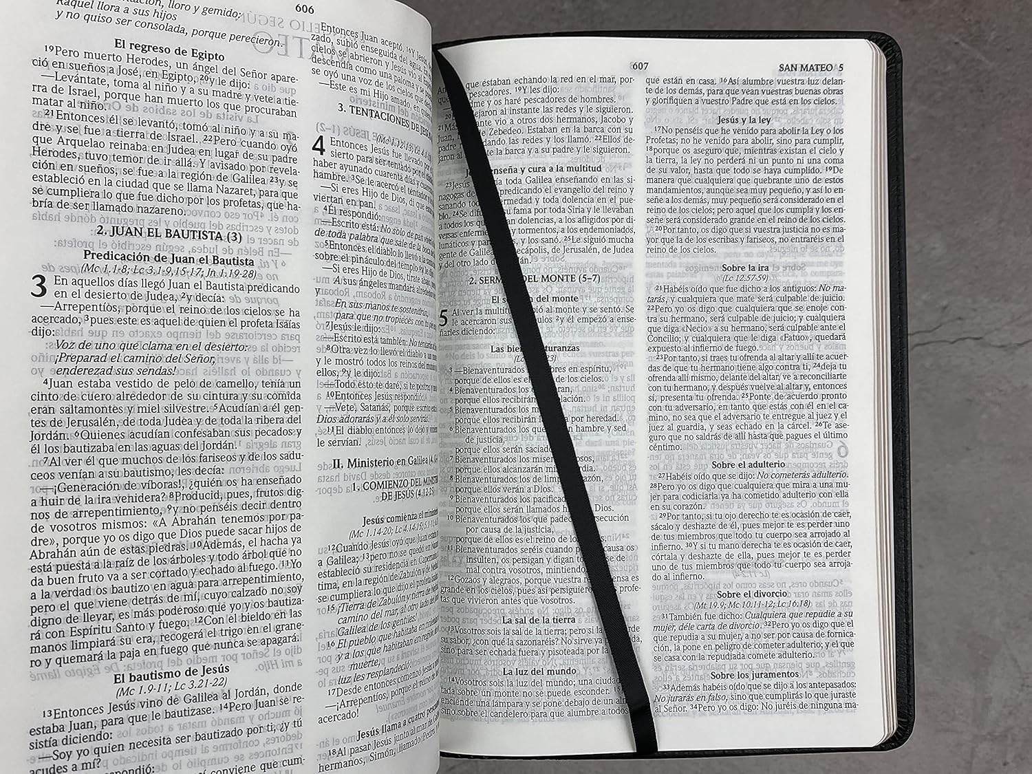 Una Biblia «ultrafina» Reina Valera 2020 en español, abierta, yace sobre una superficie gris, con una cinta negra colocada en diagonal a través de las páginas a modo de marcapáginas.