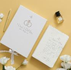 Dos cuadernos blancos, un bolígrafo, un frasco pequeño de tinta y unas flores blancas —perfectamente dispuestas sobre un fondo amarillo— evocan la elegancia de una Biblia matrimonial Reina Valera 1960 en imitación de piel blanca.