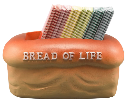 Un recipiente de plástico con forma de barra de pan y con la etiqueta «PAN DE VIDA» contiene una pila de tarjetas con versículos bíblicos de varios colores.