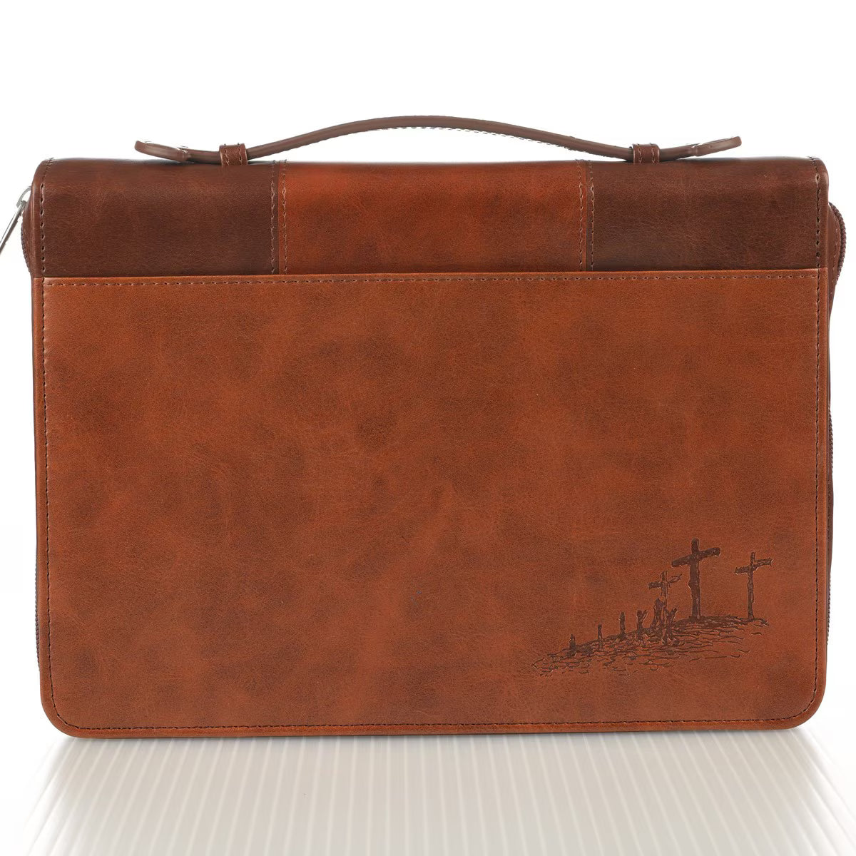 Bolso tipo maletín de cuero marrón con asa, que presenta una pequeña ilustración en relieve de tres cruces sobre una colina en la esquina inferior derecha. Esta elegante funda es perfecta para llevar tu Biblia y está fabricada con cuero sintético de alta calidad para garantizar una gran durabilidad.