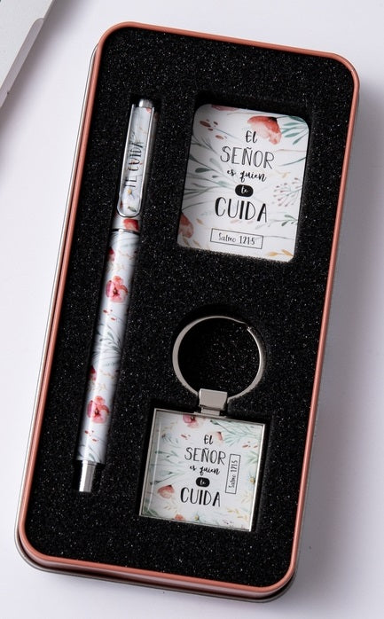 Un estuche de regalo en una caja metálica que incluye un bolígrafo con motivos florales, un bloc de notas rectangular y un llavero cuadrado, todos ellos decorados con las frases «El Señor es quien te cuida» y «Salmo 121:5».