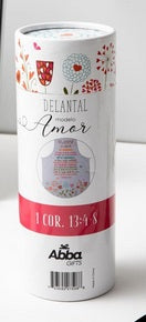 Este recipiente cilíndrico, con un diseño tubular y motivos florales decorativos, incluye un delantal de algodón con la etiqueta «Delantal modelo Amor» y una banda roja con versículos bíblicos (1 Cor. 13:4-8), de Abba Gifts.