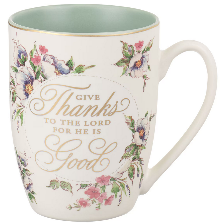 Una taza de cerámica con motivos florales y una inscripción dorada que reza: «Da gracias al Señor, porque Él es bueno», rodeada de flores pintadas, con el interior de color verde claro y una capacidad de 14 fl oz; se recomienda lavarla a mano.