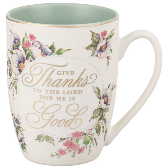 Una taza de cerámica con motivos florales y una inscripción dorada que reza: «Da gracias al Señor, porque Él es bueno», rodeada de flores pintadas, con el interior de color verde claro y una capacidad de 14 fl oz; se recomienda lavarla a mano.