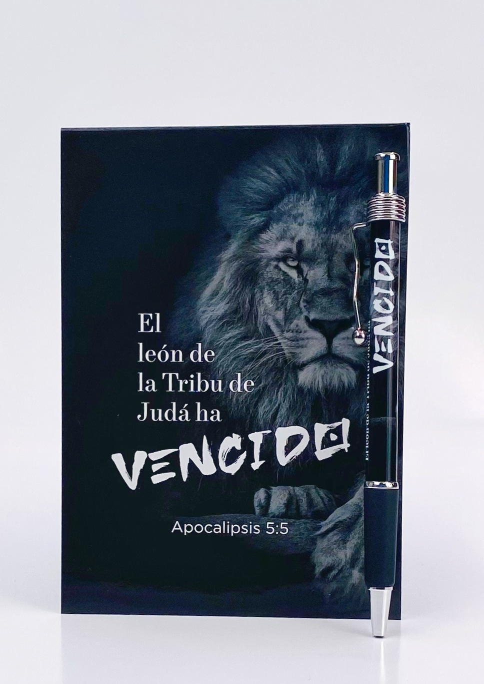 Un cuaderno negro con el León de la Tribu de Judá, con la cita bíblica «El león de la Tribu de Judá ha vencido» (Apocalipsis 5:5) en el reverso, que incluye un bolígrafo con la inscripción «VENCIDO».