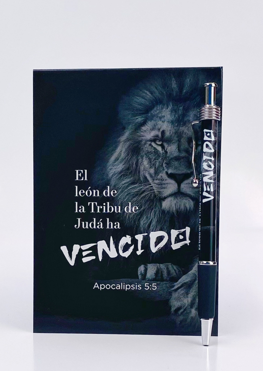 Un cuaderno negro con el León de la Tribu de Judá, con la cita bíblica «El león de la Tribu de Judá ha vencido» (Apocalipsis 5:5) en el reverso, que incluye un bolígrafo con la inscripción «VENCIDO».