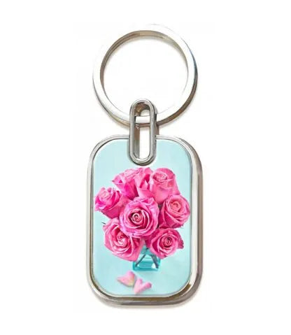 Un llavero con la imagen de un ramo de rosas rosas en un jarrón, con dos pequeñas mariposas rosas sobre un fondo azul claro, inspirado en el Salmo 121, versículo 3: «Él nunca duerme ni permite que tu pie resbale».