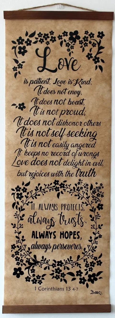 Un rollo decorativo para colgar en la pared muestra 1 Corintios 13:4-7, sobre el amor, escrito en letra cursiva y con motivos florales; es perfecto como cuadro con versículo bíblico para una bonita decoración cristiana del hogar.