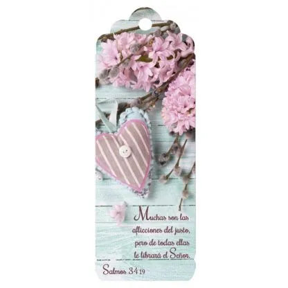 Un marcapáginas con flores rosas, un adorno en forma de corazón a rayas y el versículo «Salmos 34:19: muchas son las aflicciones del justo», extraído de la Biblia en español, descansa sobre un fondo de madera clara.