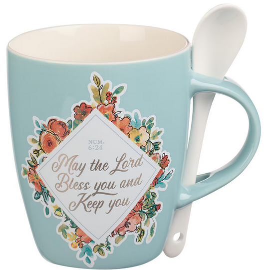 Taza azul claro de 13 fl oz con diseño floral y detalles metalizados, con la inscripción «Que el Señor te bendiga y te proteja» en la parte delantera, además de una cucharilla de cerámica colocada en el asa.