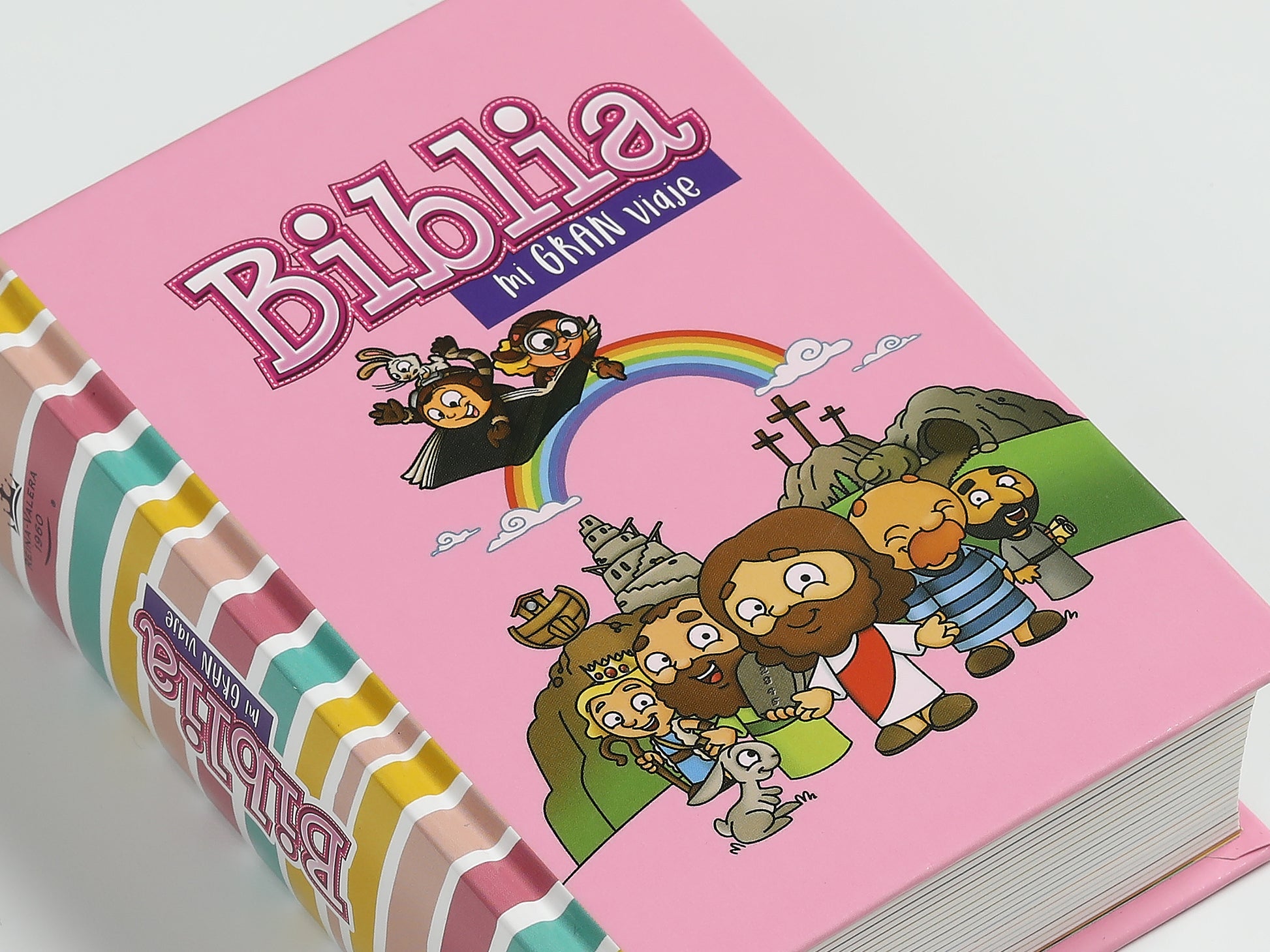Una Biblia para niños de color rosa titulada «Biblia, mi gran viaje», con dibujos bíblicos de personajes, un arcoíris y rayas de colores en el lomo, que incluye un plan de lectura bíblica.
