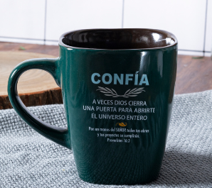 Taza de cerámica de color verde oscuro con texto en español que incluye la palabra «Confía» y un versículo bíblico, de nuestra serie de diseños únicos, colocada sobre una superficie gris con textura junto a un posavasos de madera.