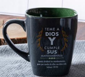 Una taza de cerámica negra de la serie «Estilos», con un texto religioso en español y hojas decorativas, sobre una superficie gris con textura.