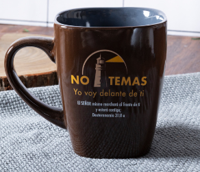 Una taza de cerámica marrón con el dibujo de un faro y un texto en español que dice «NO TEMAS. Yo voy delante de ti», además de un versículo bíblico de Deuteronomio 31:8. Disponible en varios diseños, perfecta para tu colección de tazas inspiradoras.