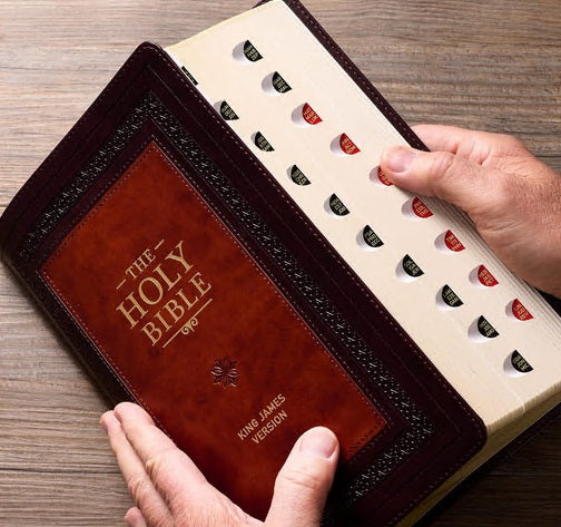Unas manos que sostienen una Biblia del Rey Jacobo, de letra grande, encuadernada en cuero y abierta, con separadores de pulgar a lo largo de los bordes de las páginas.