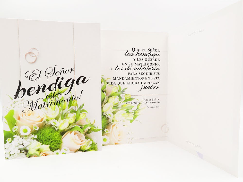 Una tarjeta de alta calidad con flores blancas y crema, anillos de boda y un texto en español en el que se bendice el matrimonio. Incluye un sobre y una funda protectora para que tus deseos lleguen a salvo a la feliz pareja.