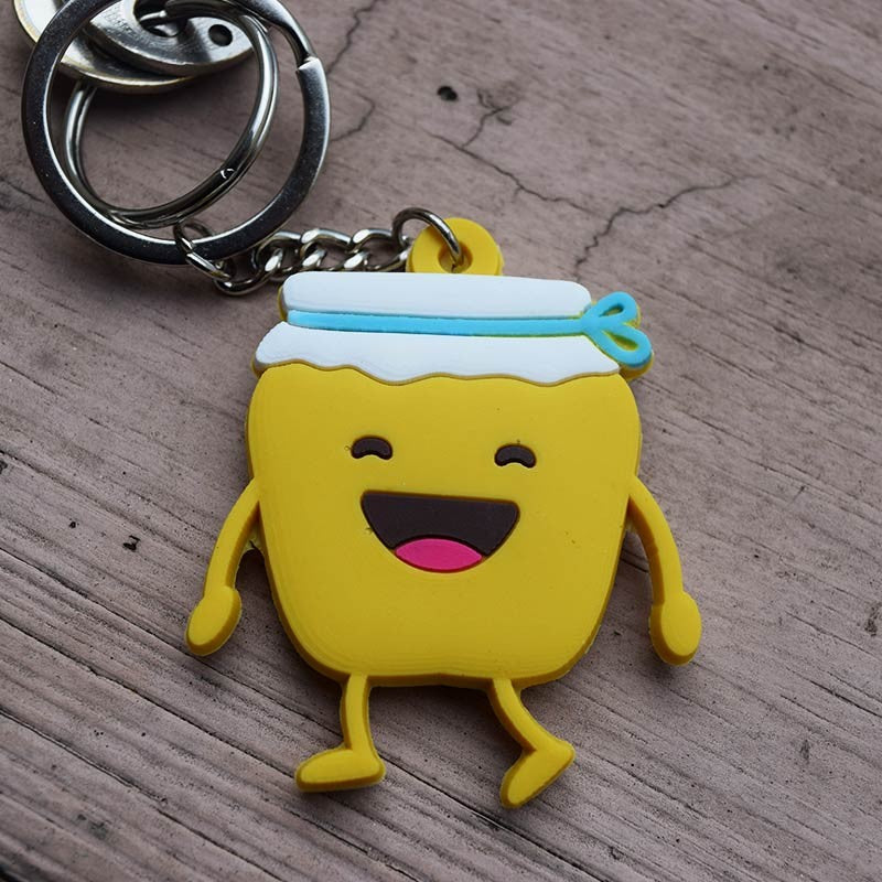 Divertido llavero con un frasco amarillo de estilo caricaturesco, una carita sonriente, una tapa blanca y una cinta azul, acompañado de la cita del Salmo 119:103; un regalo cristiano ideal sobre una base de madera.