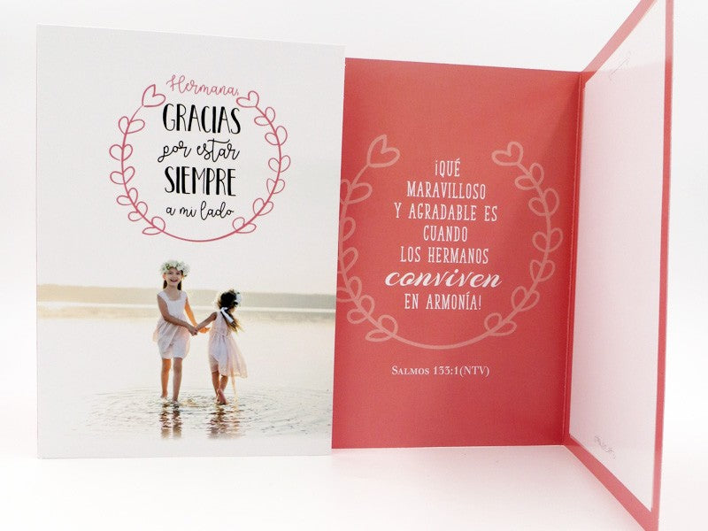 Tarjeta de felicitación con dos niñas vestidas de blanco junto al agua en la portada; en el interior, un mensaje en español sobre la armonía entre hermanos con una referencia a un versículo de la Biblia. Incluye sobre y viene en una bolsa protectora para regalarla con total seguridad.