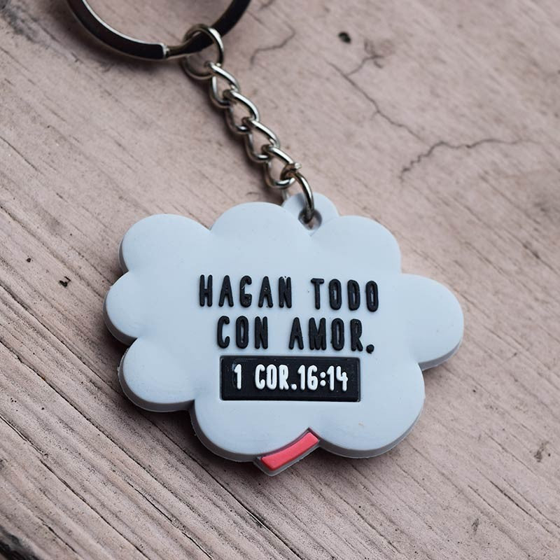 Divertido llavero con forma de nube en el que se lee la frase en español «Hagan todo con amor. 1 Corintios 16:14», apoyado sobre una superficie de madera, perfecto como regalo cristiano.