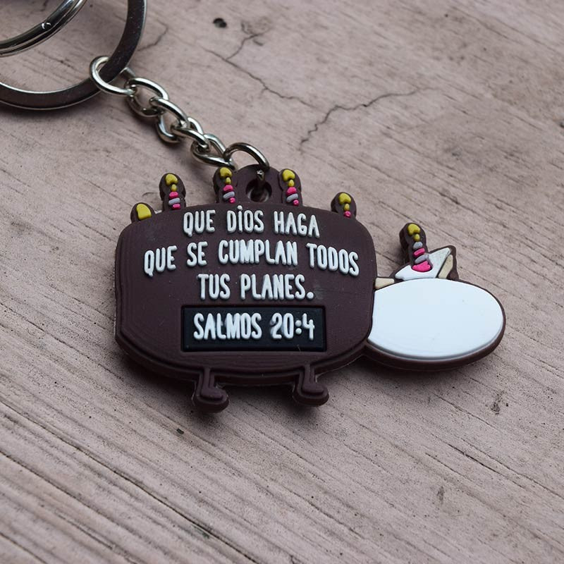 Un llavero divertido con una tarta de dibujos animados y velas, en el que se lee «Que Dios haga que se cumplan todos tus planes. Salmos 20:4» en español sobre una superficie de madera, ideal como regalo cristiano.