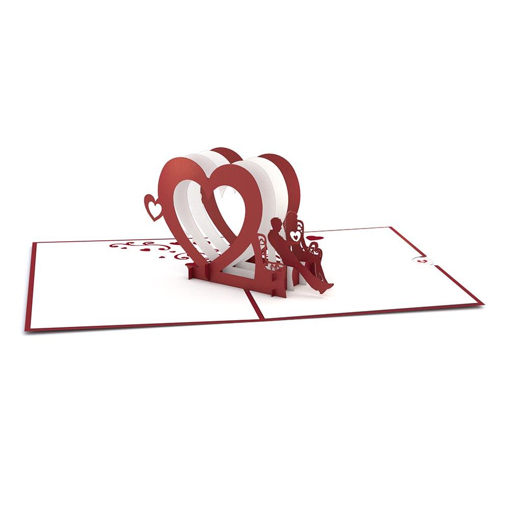Esta tarjeta pop-up de alta calidad, de 5 x 7 pulgadas, presenta corazones rojos y blancos superpuestos y la silueta de una pareja sentada en el centro.