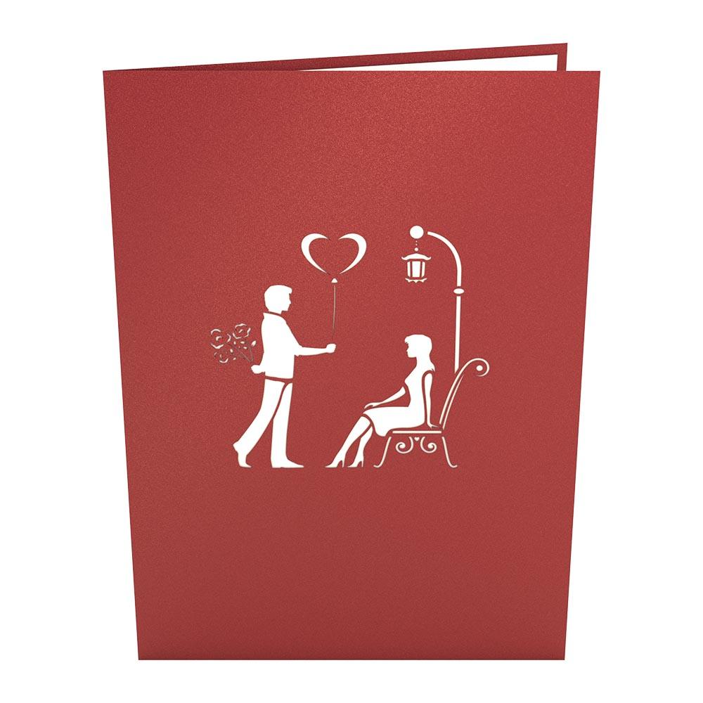 Tarjeta roja de 5 x 7 de alta calidad con diseño calado: un hombre sostiene un globo con forma de corazón y flores frente a una mujer sentada junto a una farola.