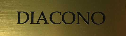 Una placa distintiva de latón con imán en la que aparece grabada la palabra «DIACONO» en mayúsculas negras.
