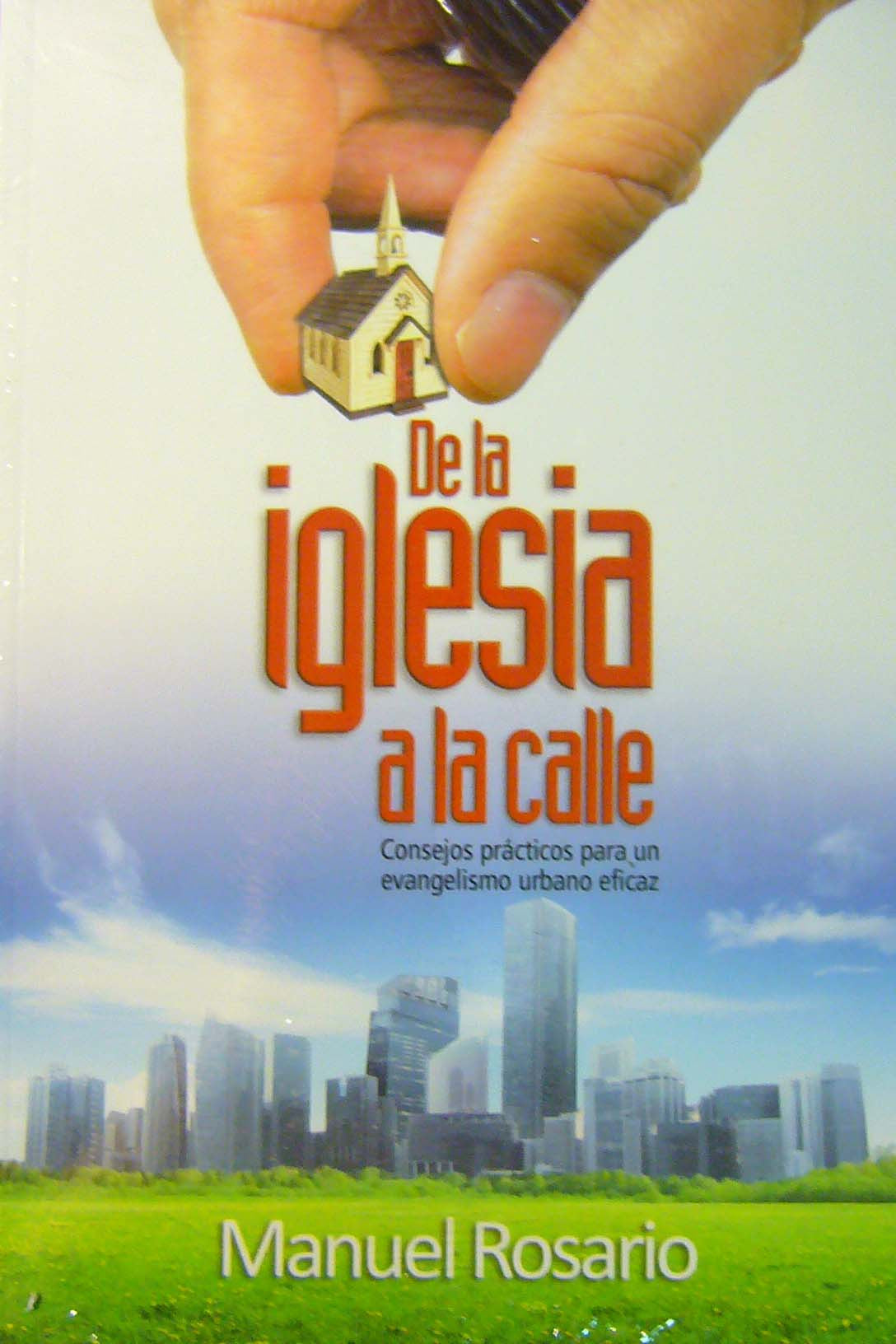 Una mano coloca una pequeña maqueta de una iglesia sobre las palabras «De la iglesia a la calle» en la portada de un libro, destacando «el evangelio eterno» en un «contexto urbano», con el perfil de la ciudad y un campo verde al fondo. Autor: Manuel Rosario.