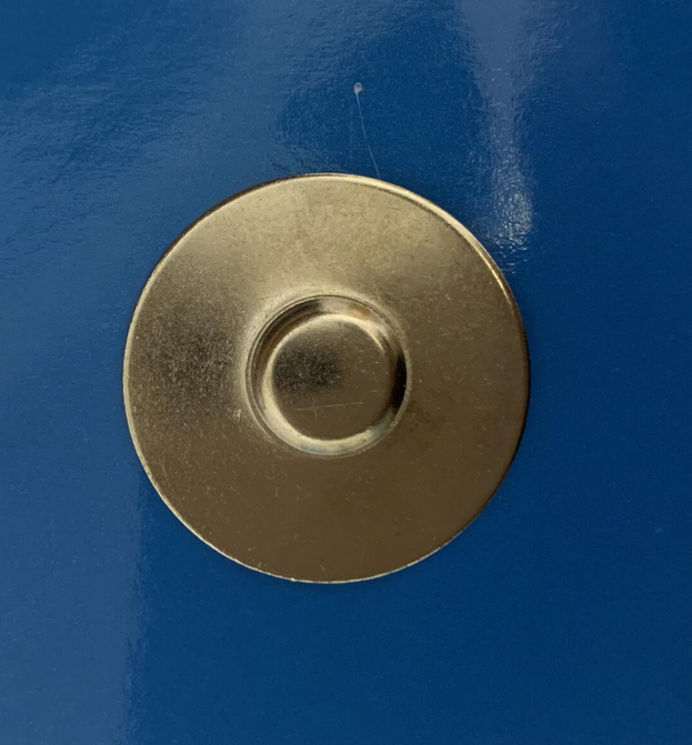 Una insignia metálica redonda y magnética está fijada a una superficie azul lisa.