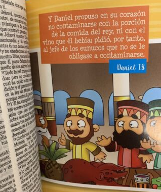 Un primer plano de una página ilustrada de una Biblia infantil en la que aparecen Daniel y otros personajes, junto con un versículo de Daniel 1:8 sobre no contaminarse con la comida y el vino del rey; ideal para los mapas bíblicos de los niños o para un plan de lectura de la Biblia en un año.