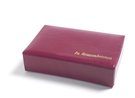 Una caja marrón cerrada, con las palabras «In Remembrance» impresas en letras doradas en la tapa, colocada sobre una superficie blanca, contiene un juego de comunión que incluye vasos desechables.