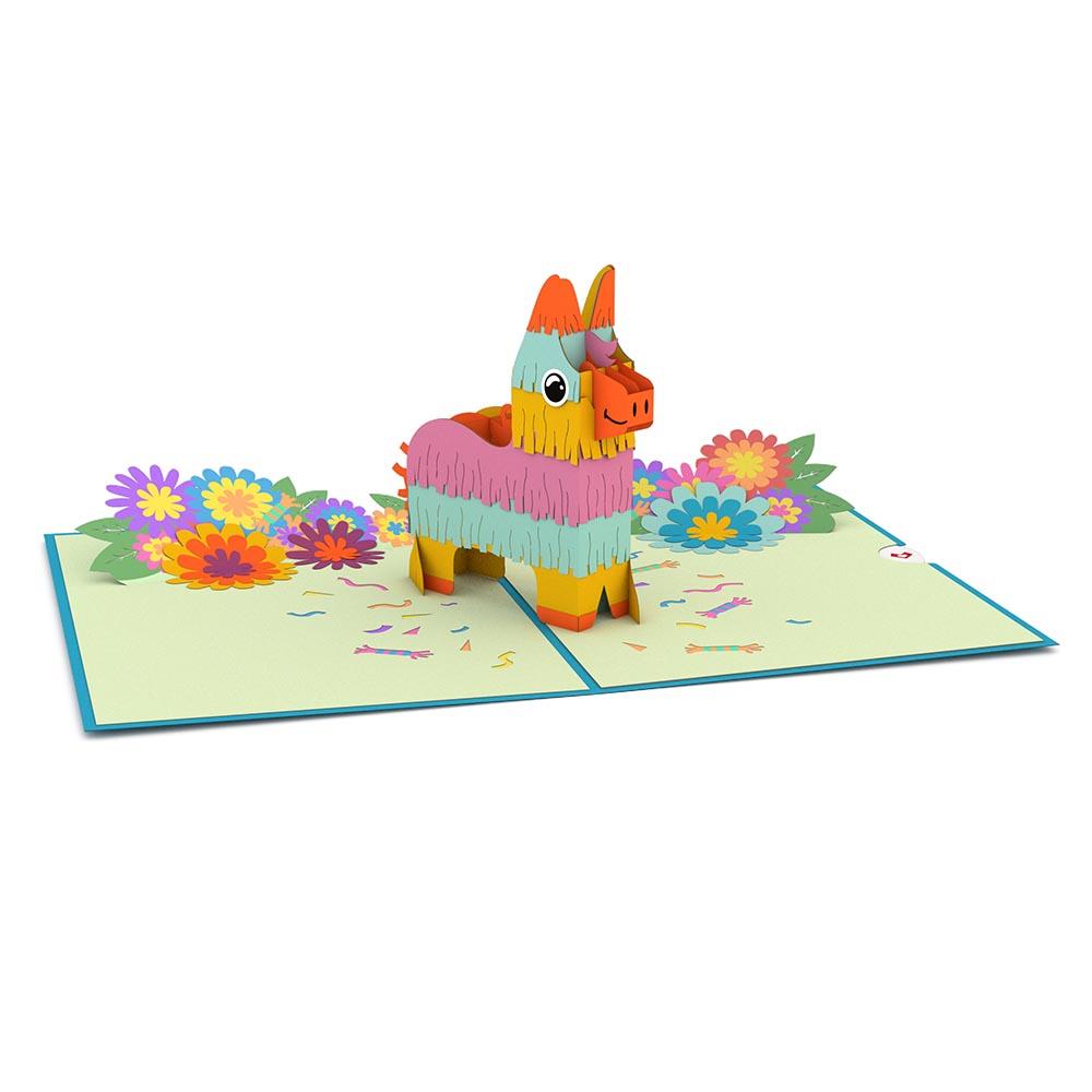 Una colorida tarjeta pop-up de 5 x 7 pulgadas en la que aparece una piñata de pie rodeada de confeti de papel y flores brillantes y multicolores sobre una superficie plana y abierta.
