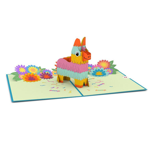 Una colorida tarjeta pop-up de 5 x 7 pulgadas en la que aparece una piñata de pie rodeada de confeti de papel y flores brillantes y multicolores sobre una superficie plana y abierta.