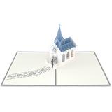 Una tarjeta de felicitación pop-up de 5 x 7 en la que aparece una iglesia blanca en tres dimensiones, con tejado y campanario azules, sobre una página en blanco.