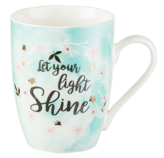 Una taza de cerámica blanca con fondo azul claro y motivos florales, en la que destaca el texto «Let your light shine» escrito en letra cursiva negra: una preciosa taza floral ideal para cualquier caja de regalo.